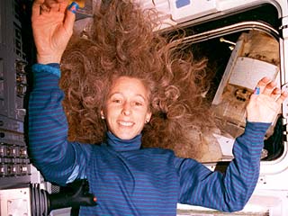 Candid views of STS-81 mission specialist Marsha Ivins (hair loose) floating on the Atlantis's aft flight deck, with the Mir space station visible in the overhead windows. 